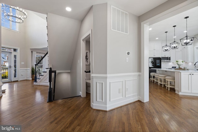 interior space with visible vents, dark wood-type flooring, stairs, wainscoting, and an inviting chandelier