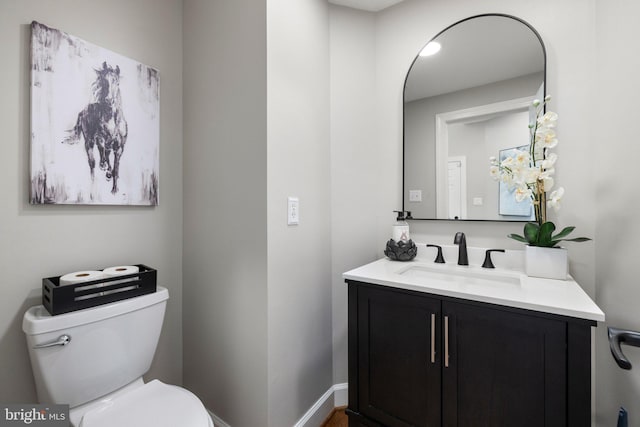 half bathroom featuring vanity, toilet, and baseboards