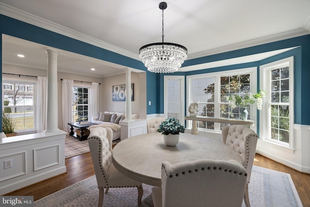 dining room featuring wood finished floors, wainscoting, and ornate columns