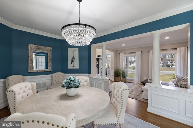 dining room featuring decorative columns, wood finished floors, wainscoting, and ornamental molding