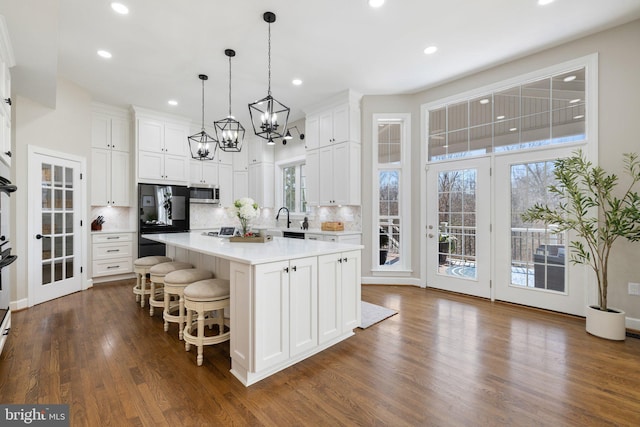 kitchen with black refrigerator, stainless steel microwave, white cabinets, light countertops, and dark wood-style flooring