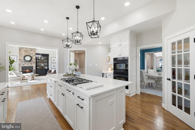 kitchen with a stone fireplace, stainless steel gas cooktop, dark wood-style flooring, and dobule oven black