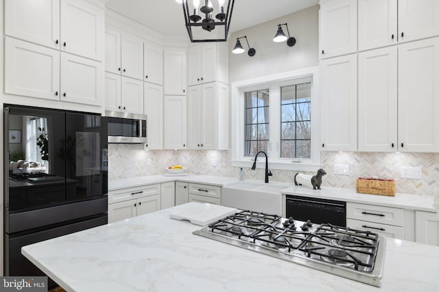 kitchen with black appliances, a sink, white cabinetry, decorative backsplash, and light stone countertops