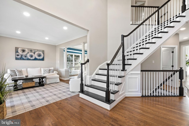 staircase with ornamental molding, wood finished floors, recessed lighting, a high ceiling, and decorative columns