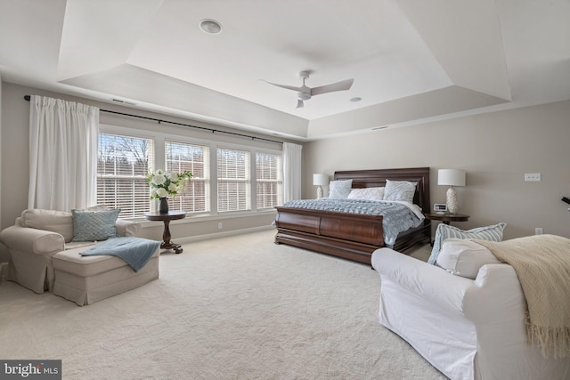 carpeted bedroom with a tray ceiling, a ceiling fan, and baseboards