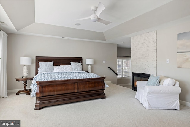 bedroom with a stone fireplace, baseboards, a tray ceiling, and carpet floors