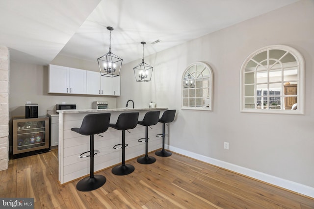 kitchen with beverage cooler, a kitchen breakfast bar, wood finished floors, white cabinets, and baseboards