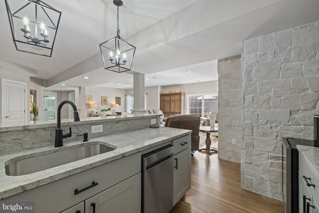 kitchen featuring light stone countertops, a sink, open floor plan, dishwasher, and light wood-type flooring