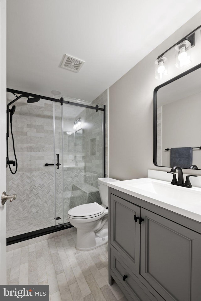 bathroom with visible vents, toilet, vanity, and a shower stall