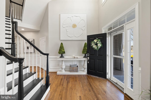 foyer entrance with stairway, wood finished floors, and a towering ceiling