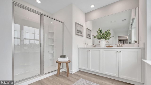 full bathroom with double vanity, recessed lighting, a stall shower, a sink, and wood finished floors