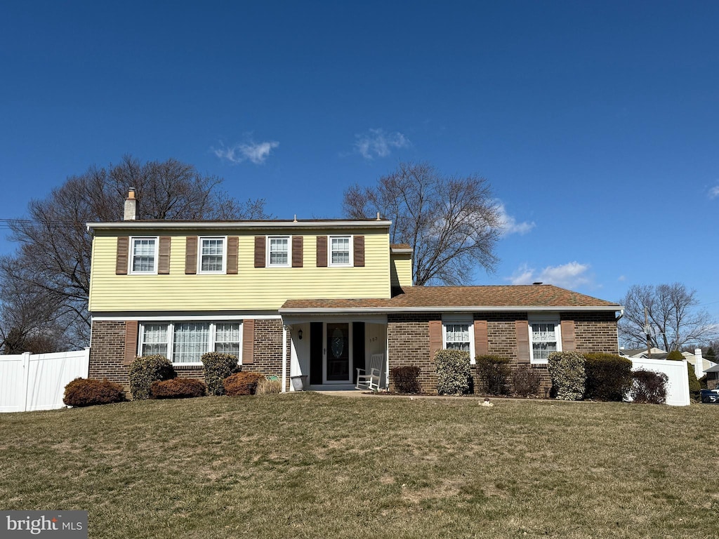 colonial inspired home with brick siding, fence, and a front lawn