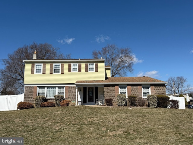 colonial house featuring brick siding, a front lawn, and fence