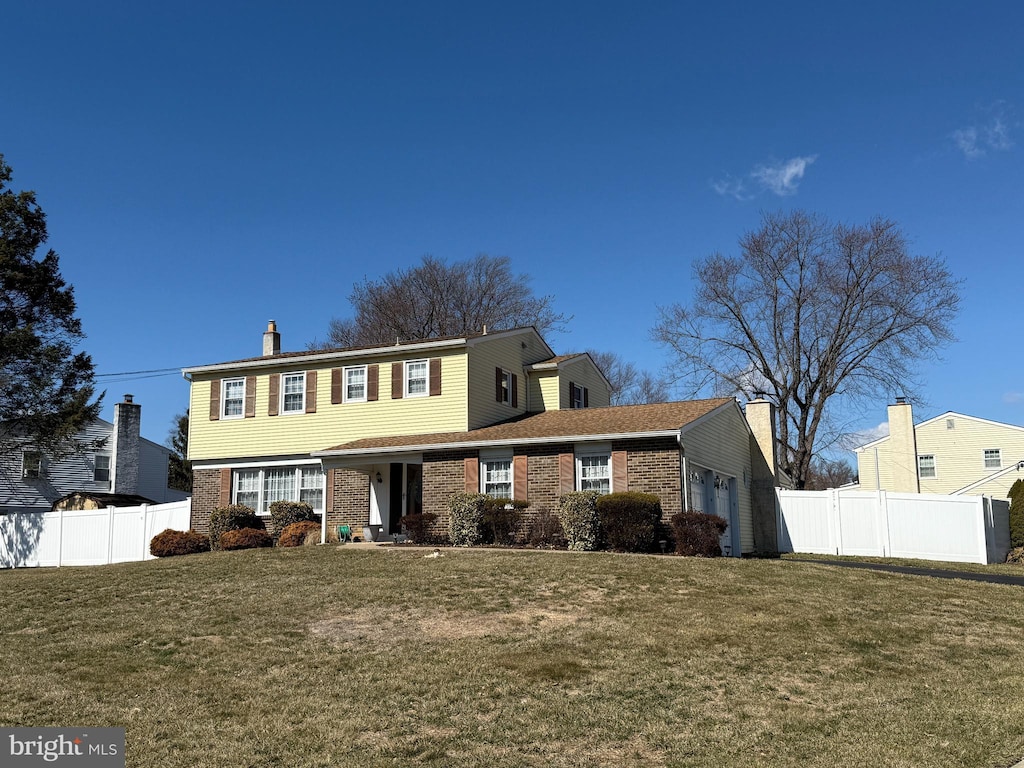 colonial inspired home with brick siding, a chimney, an attached garage, fence, and a front lawn