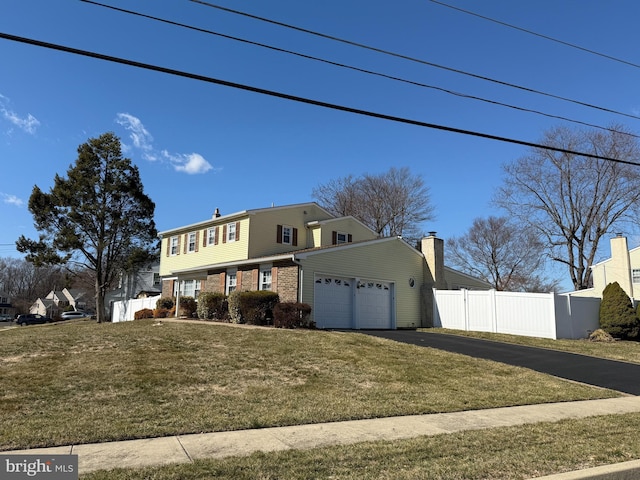 colonial-style house with aphalt driveway, a garage, brick siding, fence, and a front lawn