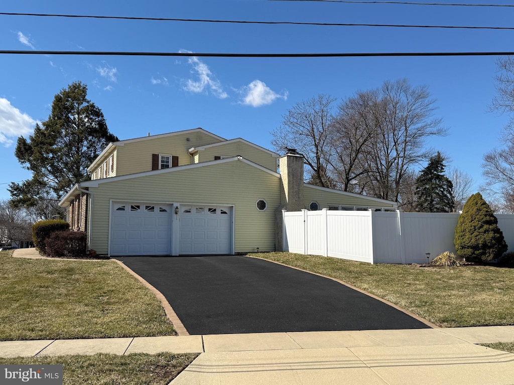 view of property exterior featuring driveway, a yard, an attached garage, and fence