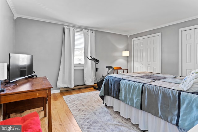 bedroom with crown molding, light wood-type flooring, and two closets