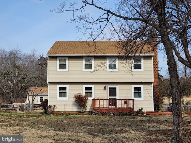 colonial-style house featuring a deck, a chimney, and a front yard