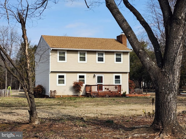 colonial house with roof with shingles, a front lawn, a chimney, and a wooden deck