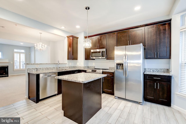 kitchen with a peninsula, stainless steel appliances, dark brown cabinets, pendant lighting, and a sink