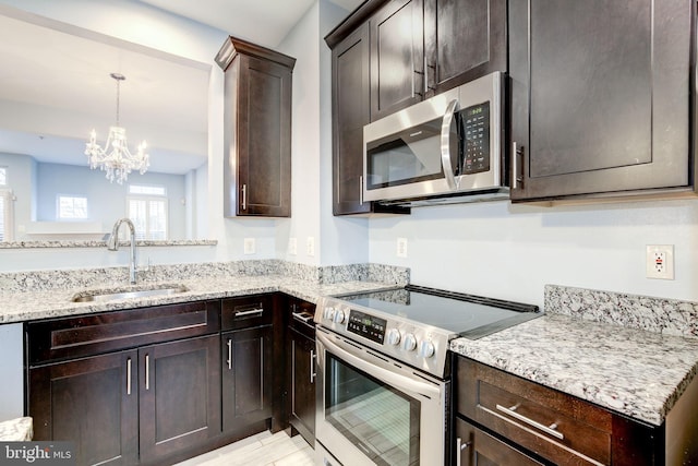 kitchen featuring dark brown cabinets, light stone counters, stainless steel appliances, and a sink