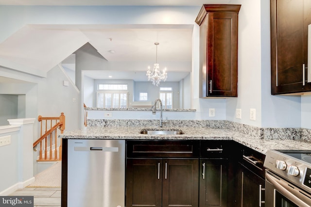 kitchen featuring dark brown cabinetry, a peninsula, a sink, appliances with stainless steel finishes, and light stone countertops