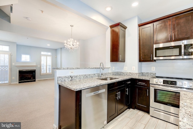 kitchen with appliances with stainless steel finishes, open floor plan, light stone countertops, a fireplace, and a sink