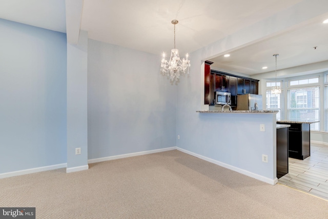 kitchen with baseboards, light colored carpet, stainless steel appliances, pendant lighting, and a notable chandelier