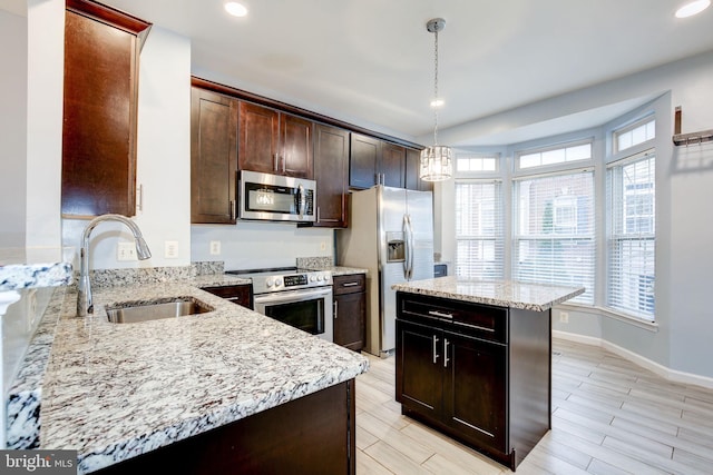 kitchen featuring appliances with stainless steel finishes, a sink, a center island, and light stone countertops