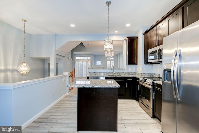 kitchen with light stone counters, stainless steel appliances, a sink, a center island, and decorative light fixtures