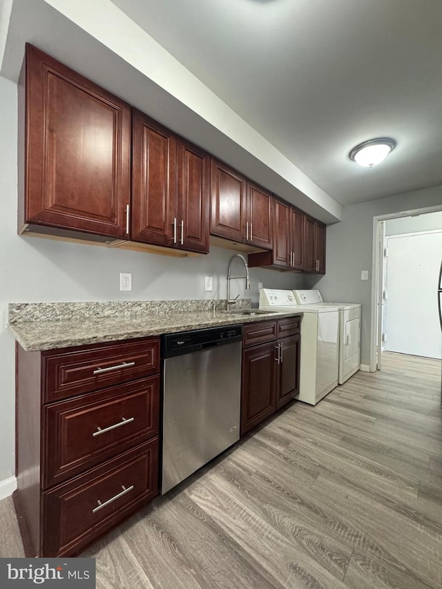 kitchen with a sink, washer and dryer, stainless steel dishwasher, light wood-style floors, and baseboards