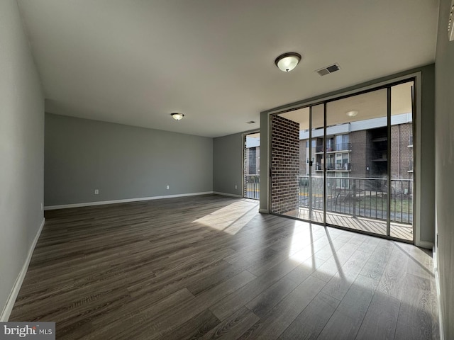 unfurnished room with floor to ceiling windows, wood finished floors, visible vents, and baseboards