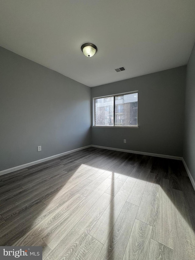 unfurnished room featuring dark wood finished floors, baseboards, and visible vents