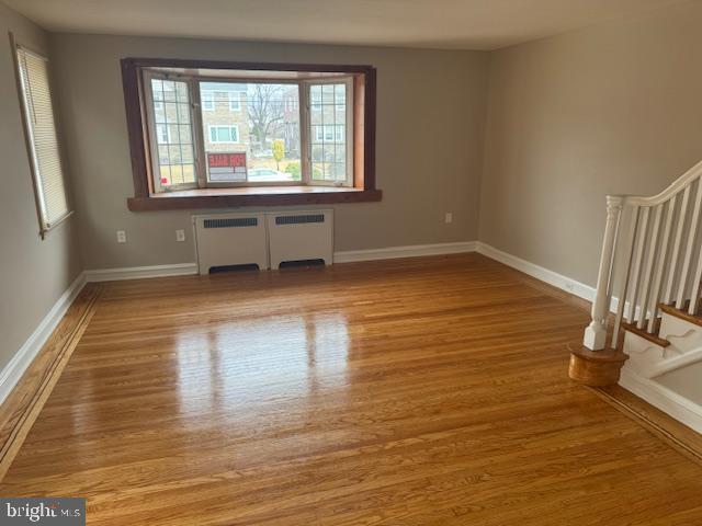 spare room featuring radiator, stairway, baseboards, and wood finished floors