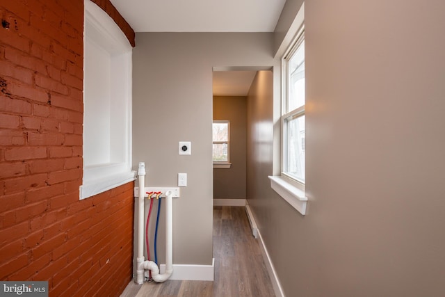 laundry room with electric dryer hookup, brick wall, wood finished floors, laundry area, and baseboards