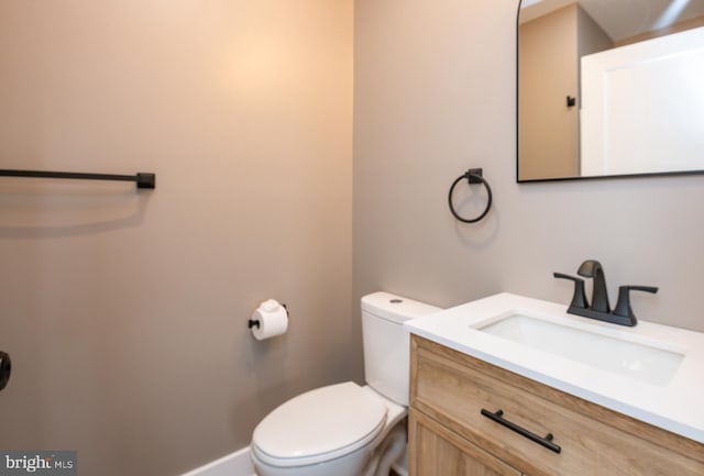 half bathroom featuring baseboards, vanity, and toilet