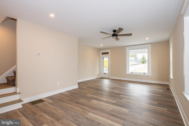 unfurnished room featuring stairs, wood finished floors, visible vents, and baseboards