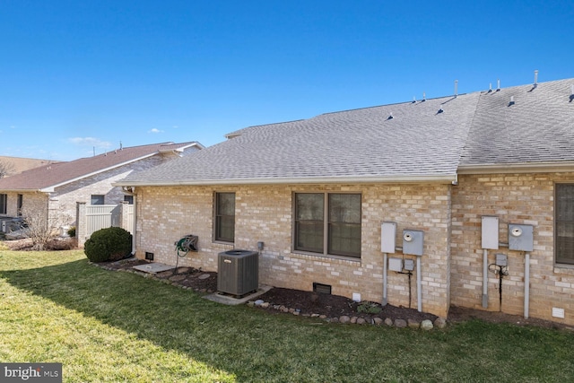 rear view of property featuring brick siding, central air condition unit, roof with shingles, a lawn, and crawl space