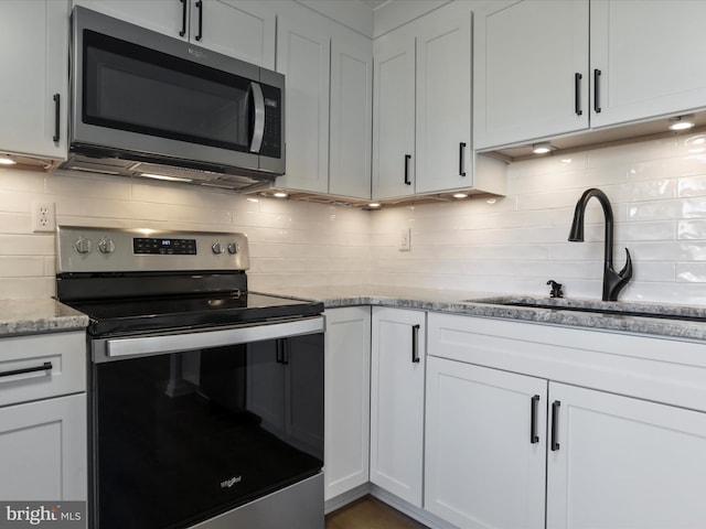 kitchen with a sink, stainless steel appliances, backsplash, and white cabinets