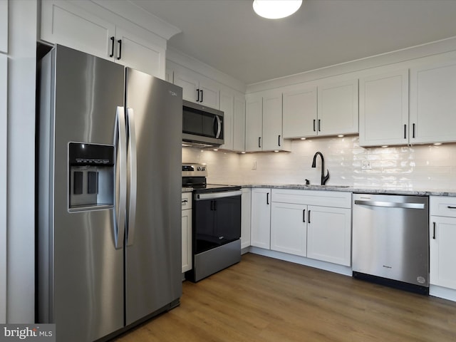 kitchen featuring wood finished floors, a sink, decorative backsplash, stainless steel appliances, and white cabinets