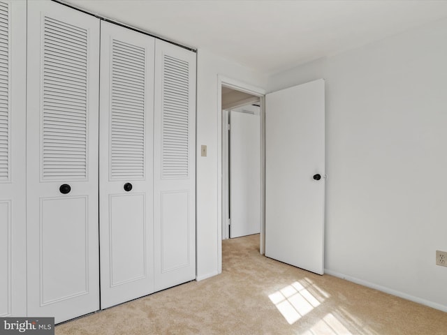 unfurnished bedroom featuring a closet, light carpet, and baseboards