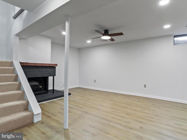 finished basement featuring a fireplace with raised hearth, ceiling fan, stairway, recessed lighting, and wood finished floors