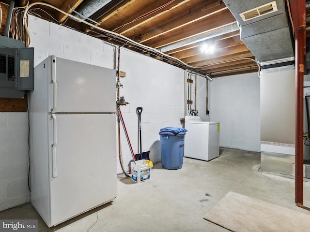 unfinished below grade area featuring electric panel, washer / clothes dryer, visible vents, and freestanding refrigerator