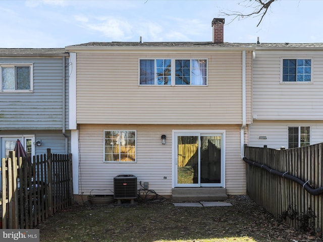 back of house featuring central AC, a fenced backyard, and a chimney