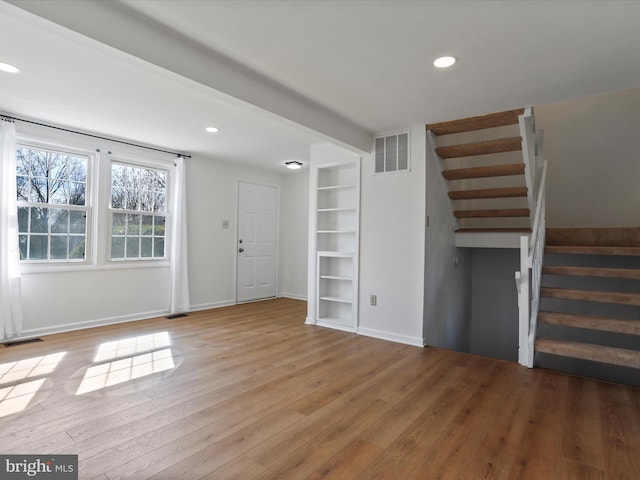 unfurnished living room with visible vents, stairway, baseboards, and wood finished floors