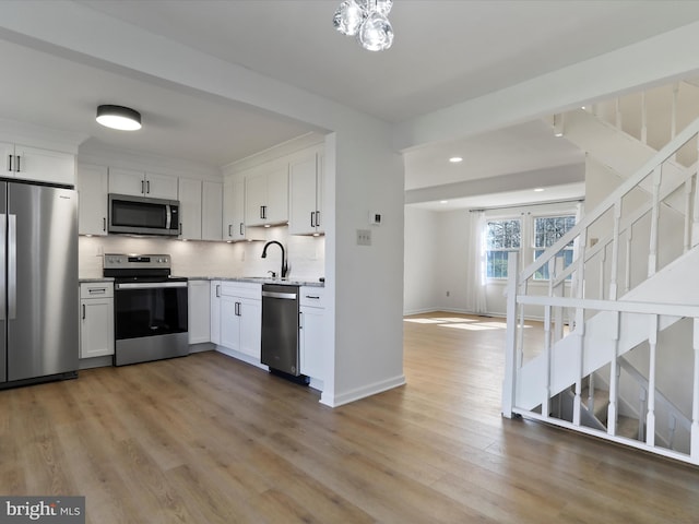 kitchen featuring stainless steel appliances, light wood-style floors, decorative backsplash, and white cabinetry