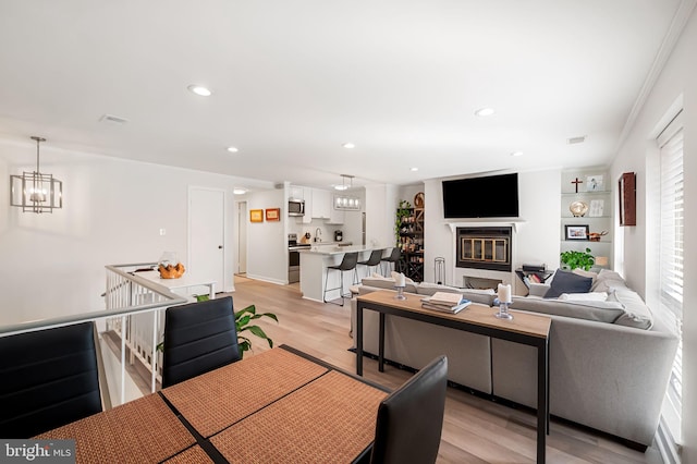 living area with a chandelier, a glass covered fireplace, light wood-style flooring, and recessed lighting