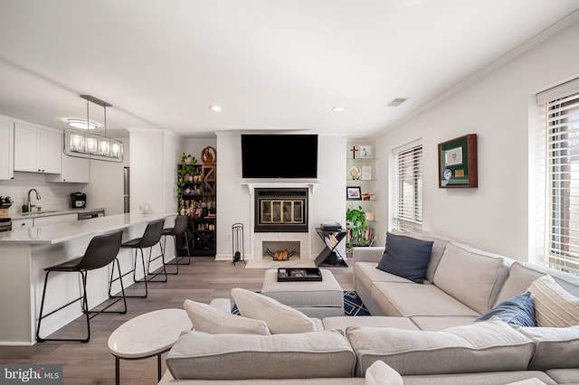 living area with crown molding, recessed lighting, light wood-style flooring, a glass covered fireplace, and a chandelier