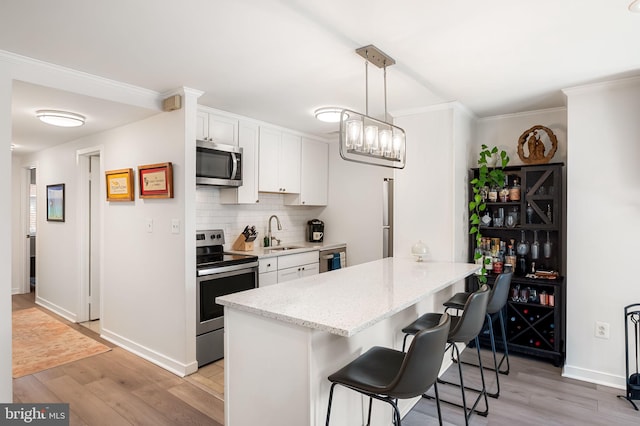 kitchen featuring decorative backsplash, appliances with stainless steel finishes, a peninsula, light wood-style floors, and a sink