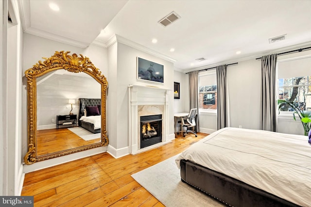 bedroom with a high end fireplace, visible vents, baseboards, ornamental molding, and hardwood / wood-style floors